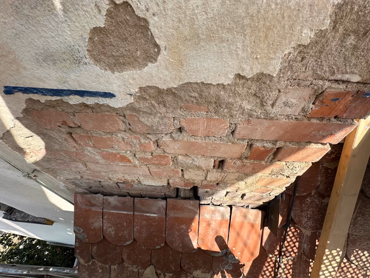 Schadstelle am Kirchturm vor der Sanierung: abgeplatzter Putz und freiliegendes Ziegelmauerwerk